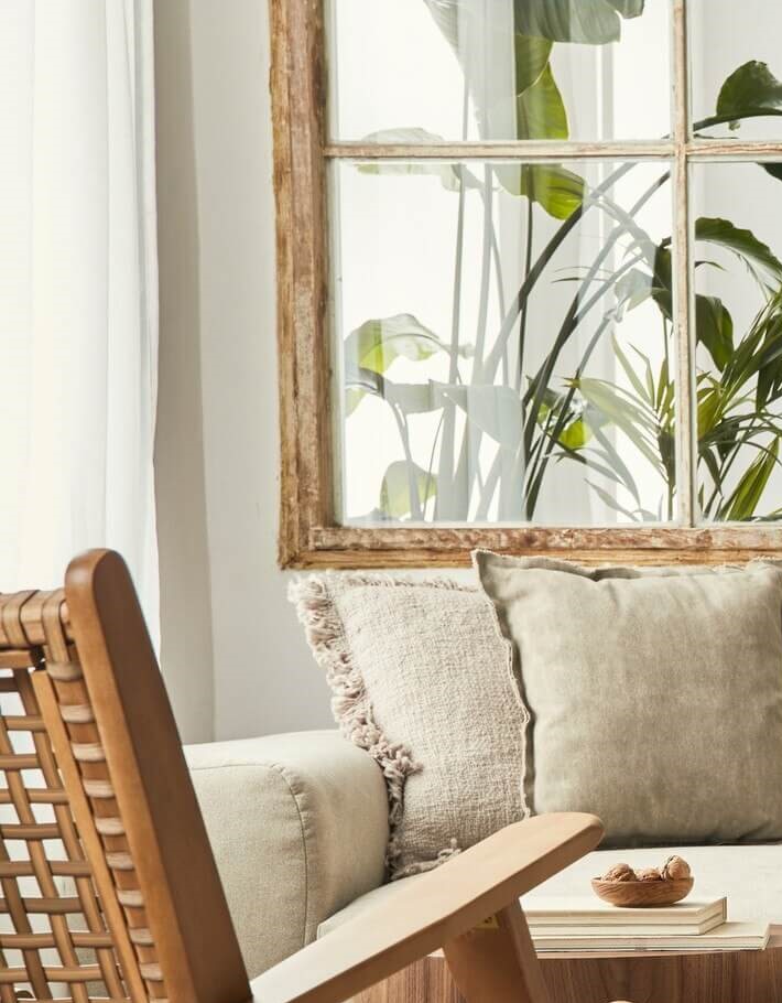 ベージュのソファにグリーンのクッションと植物が配置された、ナチュラルで温かみのあるリビングルームのインテリア画像